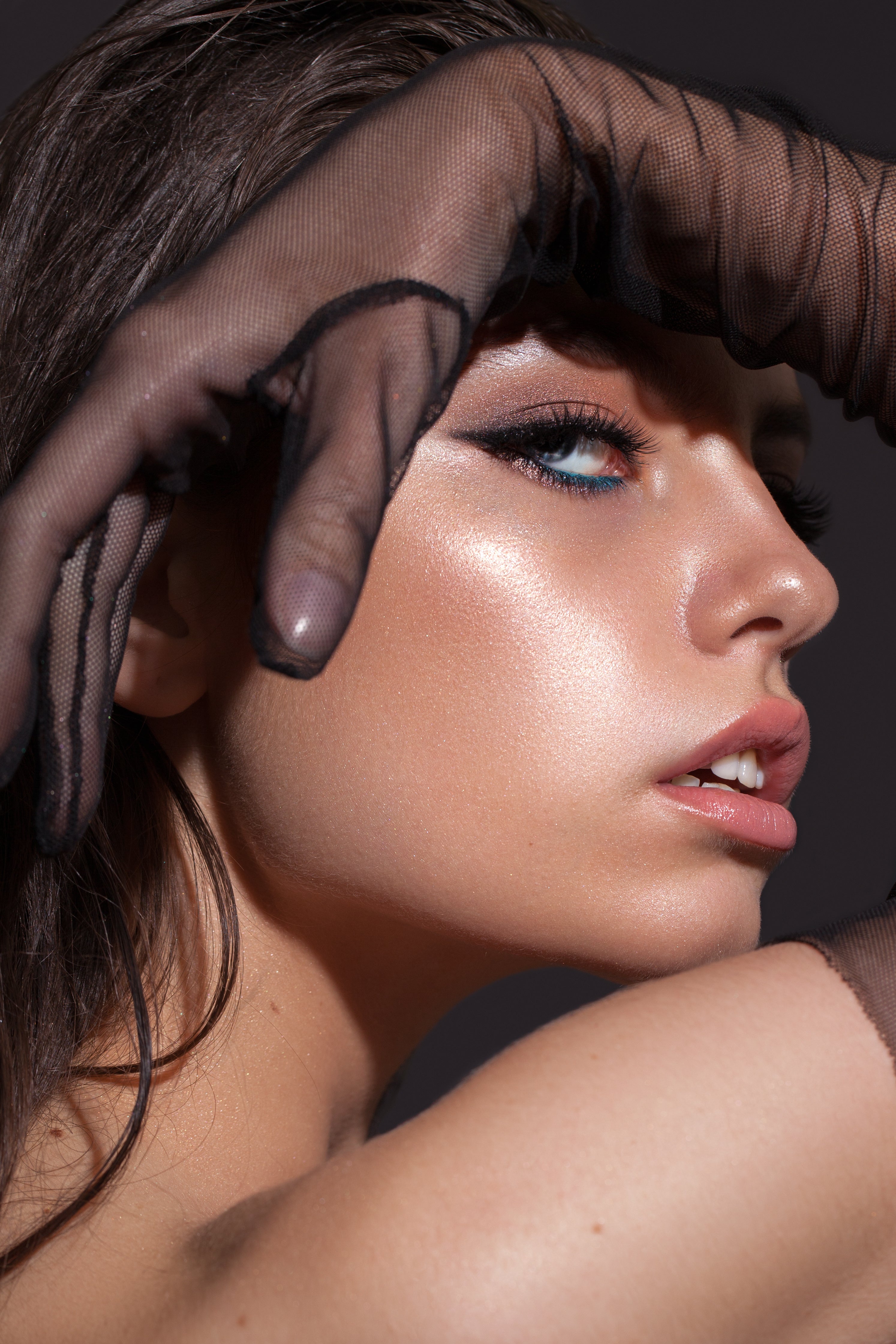 Close up of a model's face wearing blue and black liner and a glowy foundation.